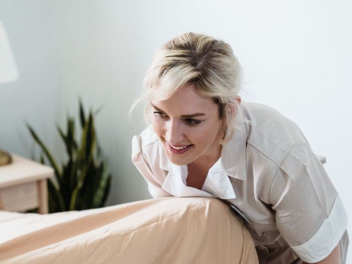 Trabajadora de limpieza de hotel sonriendo mientras arregla una cama
